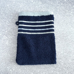 Navy cotton terry pocket washcloth with light blue stripe band and hanging loop, displayed on a speckled surface.