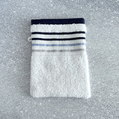 White cotton terry pocket washcloth with blue stripe band, folded neatly on a speckled surface.
