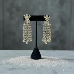 Vintage 1960s clip-on earrings with cascading clear rhinestone dangles, featuring chaton and baguette stones in a waterfall design, displayed on a black stand.