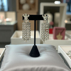 Vintage 1960s clip-on earrings with cascading clear rhinestone dangles, featuring chaton and baguette stones in a waterfall design, displayed on a black stand.