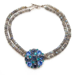  A stunning vintage Weiss crystal dome brooch in shades of blue and teal, paired with a double strand of shiny blue and gray faceted labradorite rondelles. The brooch can be worn centered, off-center, or separately, offering versatile styling. Finished with sterling silver spacers and a toggle clasp, this unique piece blends vintage charm with modern craftsmanship, signed Weiss on the back and featuring the EM tag in Etruscan alphabet for Elisabeth Michel-Meyrueix.
