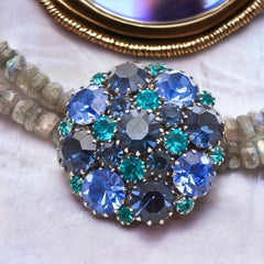  A stunning vintage Weiss crystal dome brooch in shades of blue and teal, paired with a double strand of shiny blue and gray faceted labradorite rondelles. The brooch can be worn centered, off-center, or separately, offering versatile styling. Finished with sterling silver spacers and a toggle clasp, this unique piece blends vintage charm with modern craftsmanship, signed Weiss on the back and featuring the EM tag in Etruscan alphabet for Elisabeth Michel-Meyrueix.
