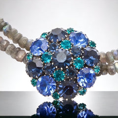  A stunning vintage Weiss crystal dome brooch in shades of blue and teal, paired with a double strand of shiny blue and gray faceted labradorite rondelles. The brooch can be worn centered, off-center, or separately, offering versatile styling. Finished with sterling silver spacers and a toggle clasp, this unique piece blends vintage charm with modern craftsmanship, signed Weiss on the back and featuring the EM tag in Etruscan alphabet for Elisabeth Michel-Meyrueix.
