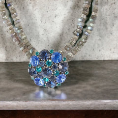  A stunning vintage Weiss crystal dome brooch in shades of blue and teal, paired with a double strand of shiny blue and gray faceted labradorite rondelles. The brooch can be worn centered, off-center, or separately, offering versatile styling. Finished with sterling silver spacers and a toggle clasp, this unique piece blends vintage charm with modern craftsmanship, signed Weiss on the back and featuring the EM tag in Etruscan alphabet for Elisabeth Michel-Meyrueix.
