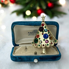 Vintage gold-tone Christmas tree brooch with multicolor rhinestones and scalloped edges, featuring a star at the top and textured detailing; back view shows pin clasp and trunk-shaped base, typical of 1980s–1990s holiday jewelry.