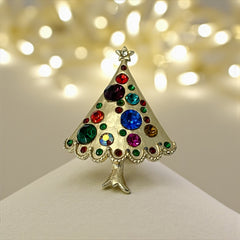 Vintage gold-tone Christmas tree brooch with multicolor rhinestones and scalloped edges, featuring a star at the top and textured detailing; back view shows pin clasp and trunk-shaped base, typical of 1980s–1990s holiday jewelry.