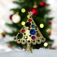 Vintage gold-tone Christmas tree brooch with multicolor rhinestones and scalloped edges, featuring a star at the top and textured detailing; back view shows pin clasp and trunk-shaped base, typical of 1980s–1990s holiday jewelry.