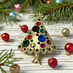 Vintage gold-tone Christmas tree brooch with multicolor rhinestones and scalloped edges, featuring a star at the top and textured detailing; back view shows pin clasp and trunk-shaped base, typical of 1980s–1990s holiday jewelry.