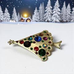 Vintage gold-tone Christmas tree brooch with multicolor rhinestones and scalloped edges, featuring a star at the top and textured detailing; back view shows pin clasp and trunk-shaped base, typical of 1980s–1990s holiday jewelry.