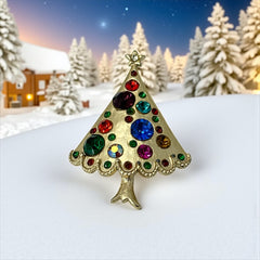Vintage gold-tone Christmas tree brooch with multicolor rhinestones and scalloped edges, featuring a star at the top and textured detailing; back view shows pin clasp and trunk-shaped base, typical of 1980s–1990s holiday jewelry.