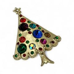 Vintage gold-tone Christmas tree brooch with multicolor rhinestones and scalloped edges, featuring a star at the top and textured detailing; back view shows pin clasp and trunk-shaped base, typical of 1980s–1990s holiday jewelry.