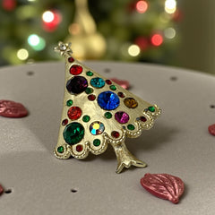 Vintage gold-tone Christmas tree brooch with multicolor rhinestones and scalloped edges, featuring a star at the top and textured detailing; back view shows pin clasp and trunk-shaped base, typical of 1980s–1990s holiday jewelry.