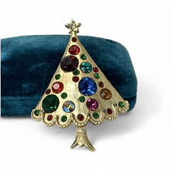 Vintage gold-tone Christmas tree brooch with multicolor rhinestones and scalloped edges, featuring a star at the top and textured detailing; back view shows pin clasp and trunk-shaped base, typical of 1980s–1990s holiday jewelry.
