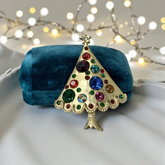 Vintage gold-tone Christmas tree brooch with multicolor rhinestones and scalloped edges, featuring a star at the top and textured detailing; back view shows pin clasp and trunk-shaped base, typical of 1980s–1990s holiday jewelry.