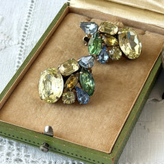 Vintage 1950s gold tone clip‑on earrings with yellow, blue, and green rhinestones in oval, pear, marquise, and emerald cuts, shown from multiple angles.