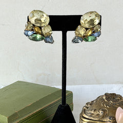 Vintage 1950s gold tone clip‑on earrings with yellow, blue, and green rhinestones in oval, pear, marquise, and emerald cuts, shown from multiple angles.