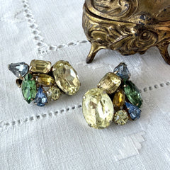 Vintage 1950s gold tone clip‑on earrings with yellow, blue, and green rhinestones in oval, pear, marquise, and emerald cuts, shown from multiple angles.