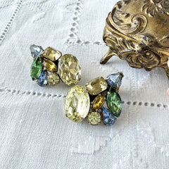 Vintage 1950s gold tone clip‑on earrings with yellow, blue, and green rhinestones in oval, pear, marquise, and emerald cuts, shown from multiple angles.