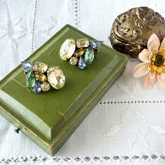 Vintage 1950s gold tone clip‑on earrings with yellow, blue, and green rhinestones in oval, pear, marquise, and emerald cuts, shown from multiple angles.