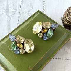 Vintage 1950s gold tone clip‑on earrings with yellow, blue, and green rhinestones in oval, pear, marquise, and emerald cuts, shown from multiple angles.