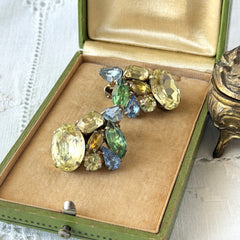 Vintage 1950s gold tone clip‑on earrings with yellow, blue, and green rhinestones in oval, pear, marquise, and emerald cuts, shown from multiple angles.