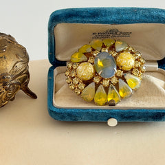 Vintage gold‑tone brooch with blue‑gray givre cabochon, yellow givre teardrops, confetti Lucite cabochons, and yellow chaton rhinestones.