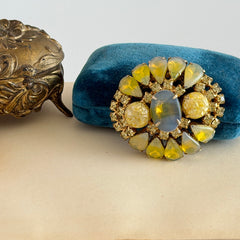Vintage gold‑tone brooch with blue‑gray givre cabochon, yellow givre teardrops, confetti Lucite cabochons, and yellow chaton rhinestones.