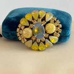 Vintage gold‑tone brooch with blue‑gray givre cabochon, yellow givre teardrops, confetti Lucite cabochons, and yellow chaton rhinestones.