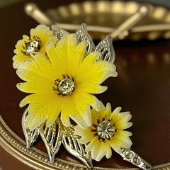 Vintage yellow celluloid floral brooch from the 1950s featuring three gradient yellow-to-white flowers with clear rhinestone centers, accented by light gold-tone openwork leaves.