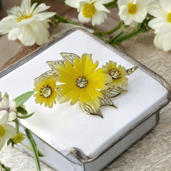 Vintage yellow celluloid floral brooch from the 1950s featuring three gradient yellow-to-white flowers with clear rhinestone centers, accented by light gold-tone openwork leaves.