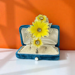 Vintage yellow celluloid floral brooch from the 1950s featuring three gradient yellow-to-white flowers with clear rhinestone centers, accented by light gold-tone openwork leaves.
