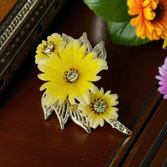 Vintage yellow celluloid floral brooch from the 1950s featuring three gradient yellow-to-white flowers with clear rhinestone centers, accented by light gold-tone openwork leaves.