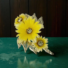 Vintage yellow celluloid floral brooch from the 1950s featuring three gradient yellow-to-white flowers with clear rhinestone centers, accented by light gold-tone openwork leaves.