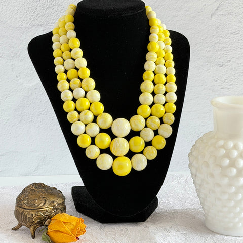 Vintage 1950s yellow three‑strand necklace with graduated cellulose acetate beads in solid and marbled tones, shown in various views to display bead details and overall design.