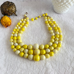 Vintage 1950s yellow three‑strand necklace with graduated cellulose acetate beads in solid and marbled tones, shown in various views to display bead details and overall design.