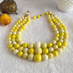 Vintage 1950s yellow three‑strand necklace with graduated cellulose acetate beads in solid and marbled tones, shown in various views to display bead details and overall design.